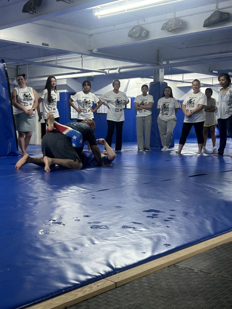 Women in Women’s Self Defense Seminar shirts stand together at North Georgia Hayastan MMA Academy in Dalton, Georgia, during a seminar with Leonardo Lechuga