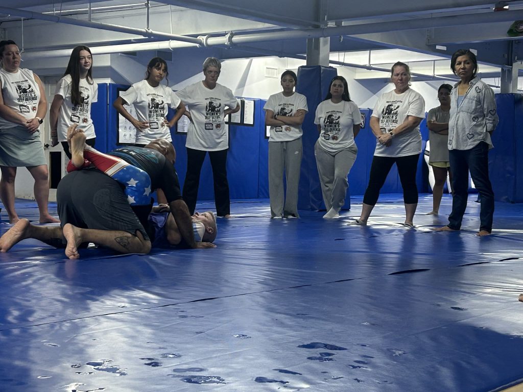 Participants in Women’s Self Defense Seminar shirts watch a ground demonstration during a women’s self-defense seminar at North Georgia Hayastan MMA Academy in Dalton, Georgia